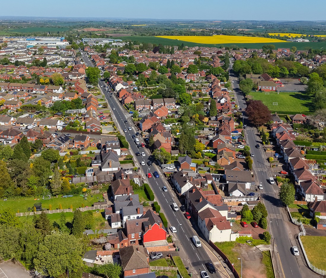 Aerial view over rooftops and tree-lined streets looking towards open countryside
